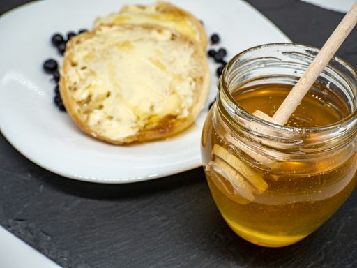 A tasty sweet pancake with cream and blackberries on a white plate near the jar of honey