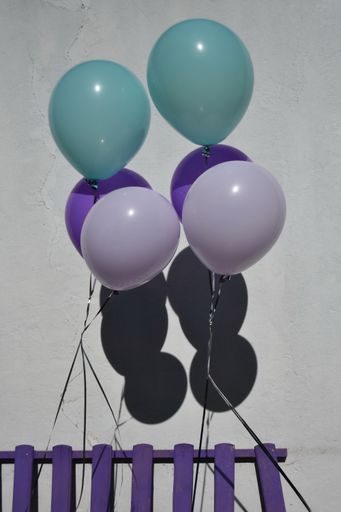 A vertical shot of six colorful balloons isolated against a white wall at a birthday party