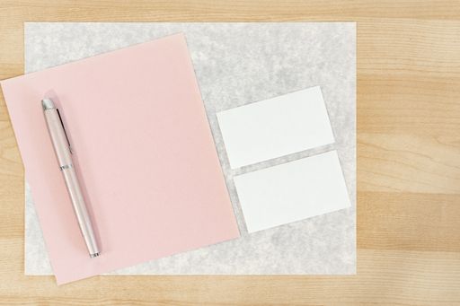 Blank pink greeting card with a rose pen and two cards on a wooden table