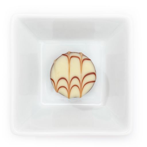 A top view of white chocolate praline in a square bowl on a white background