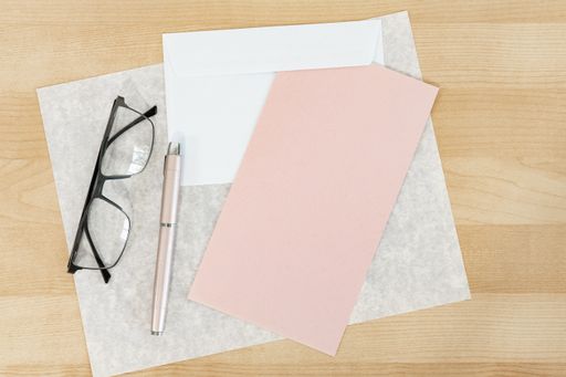 A top view shot of a wooden table with glasses over the textured, pink paper and a pen