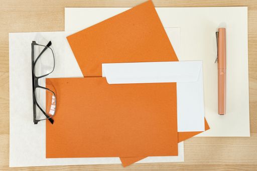 A mockup of orange paper blanks with envelope and pen on a wooden desk. Autumnal Invitation and greeting cards
