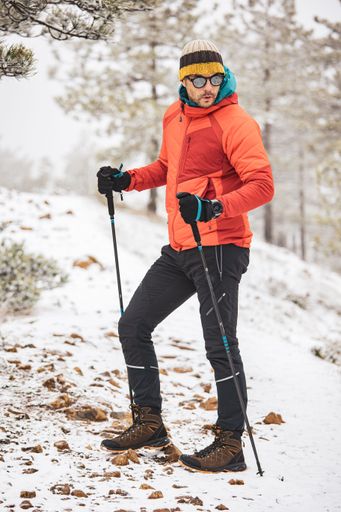 A man in winter hiking gear with trekking poles on a snowy trail in a forest