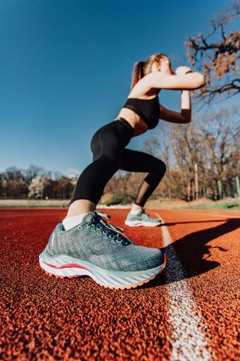 A young woman in athletic wear performs lunges on a sunny outdoor track, focusing on her shoes
