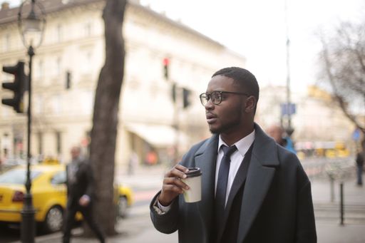 An African American male walking on the sidewalk while holding a coffee