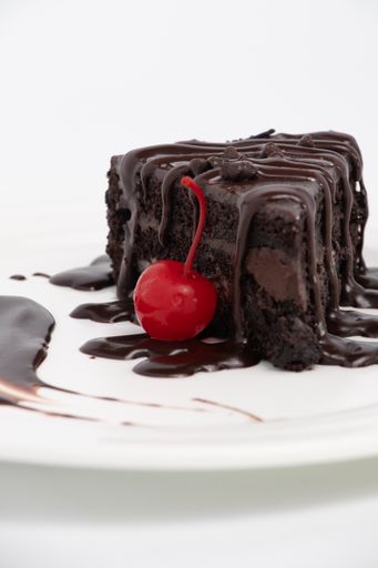 A vertical closeup shot of a delicious chocolate cake with a cherry beside it on a white plate