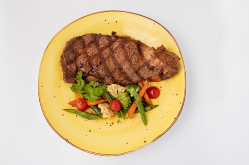 A top view of a delicious steak with vegetables in a yellow plate on a white background