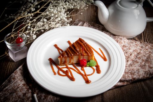 An angle shot of a cake piece served with caramel topping and a cherry.