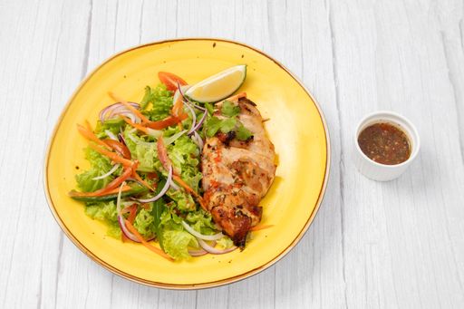 An angle top shot of a grilled chicken breast with salad on a yellow plate next to a sauce.