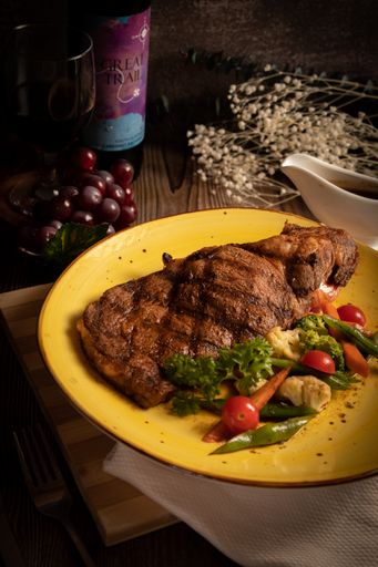 A vertical shot of a meat steak with a side dish of vegetables served on a yellow plate.
