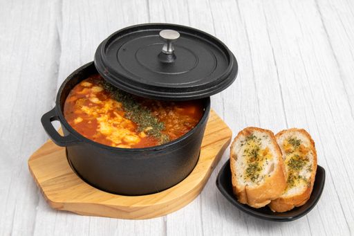 An angle shot of a soup served in a small pot next to bruschetta bread slicers.
