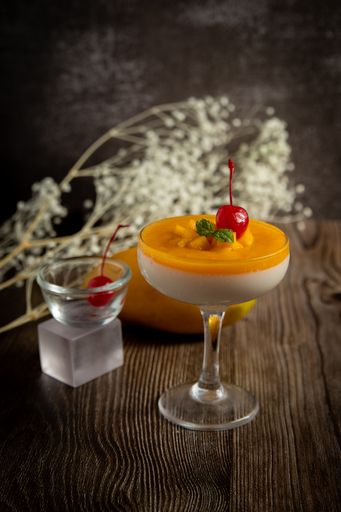 A vertical shot of a mango mousse dessert in a glass on a wooden table.