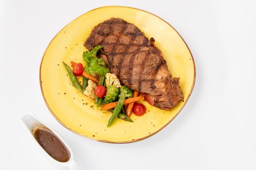 An angle top shot of a meat steak with a side dish of vegetables served on a yellow plate.