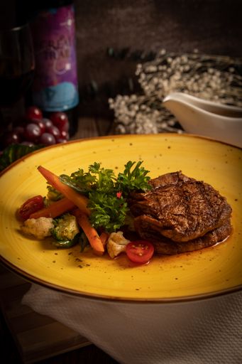 A vertical shot of a meat steak with a dish of vegetables served on a yellow plate.