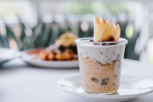 A delicious parfait with oats, yogurt, raisins, and apple slices served in a glass jar on a table.