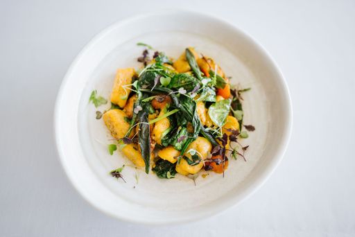 A gourmet dish featuring gnocchi with fresh greens and herbs elegantly presented in a white bowl on a light background.