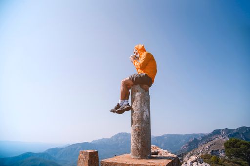 A man sitting on top of the rock and watching the valley having a cup of  coffee