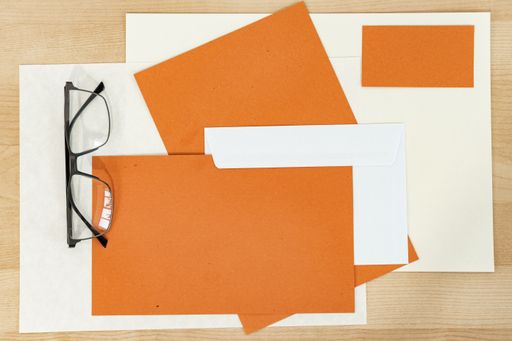 A top view shot of a wooden table with glasses, orange paper, an envelope, and a pen