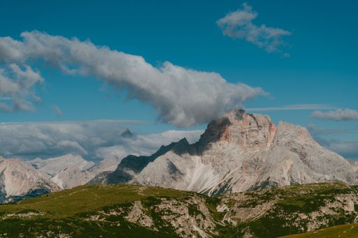 A stunning view of a mountain range under a clear blue sky with a cloud hovering over the peak.