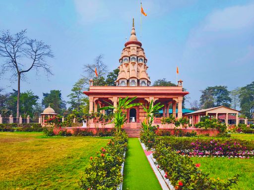 A vibrant temple with a lush garden pathway leading to its entrance, set under a clear blue sky.