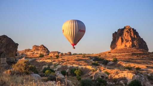 Hot air balloon soaring over the rocky landscape of Cappadocia at sunset, highlighting the unique rock formations and serene sky.
