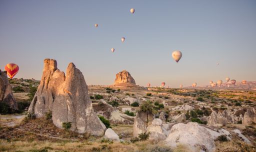 Hot air balloons soar over the unique rock formations of Cappadocia, Turkey, during a serene sunrise.