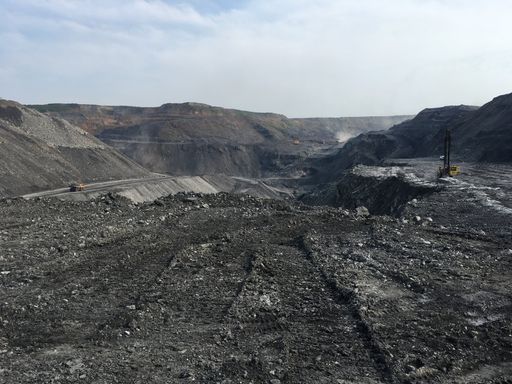 A vast open-pit mine with trucks and machinery under a clear sky, showcasing industrial landscape and mining activity.