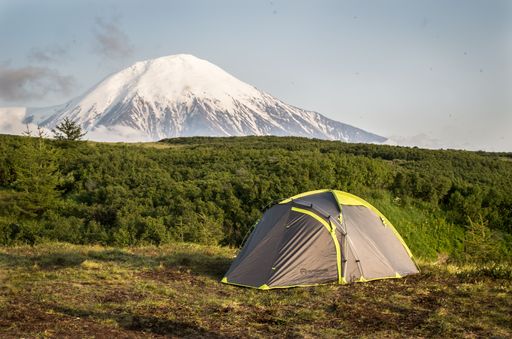 A camping tent set against the backdrop of a snow-capped mountain and lush greenery under a clear sky.
