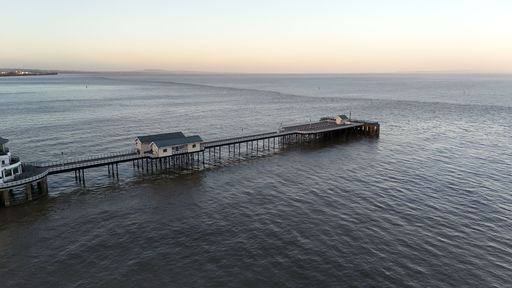 A serene view of a long pier extending into the calm sea during sunset with a clear sky in the background.
