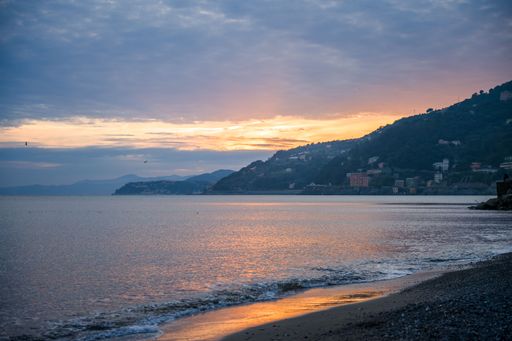Scenic coastal view at sunset with mountains and a tranquil sea reflecting warm hues in Liguria, Italy.