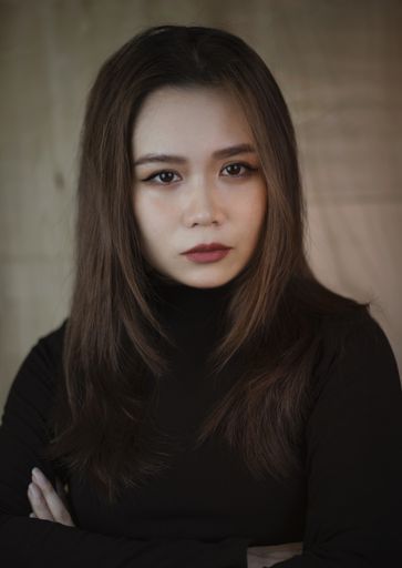 A vertical shot of a young Southeast Asian woman looking at the camera with a wooden background in Vietnam