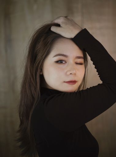 A vertical shot of a Southeast Asian girl looking at the camera with one eye closed on a wooden background in Vietnam
