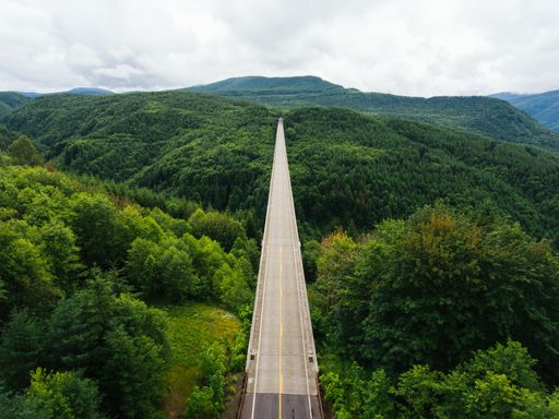 A landscape of a road surrounded by hills covered in greenery under a cloudy sky