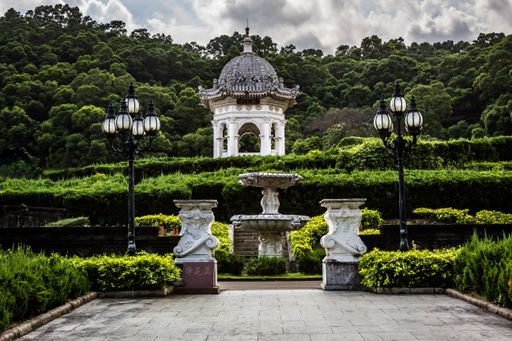A view of beautiful gardens with street lanterns and an ancient stone cupola under the cloudy sky