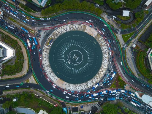 Aerial view of the iconic Bundaran HI fountain surrounded by traffic in Jakarta, Indonesia, showcasing urban life and architecture.