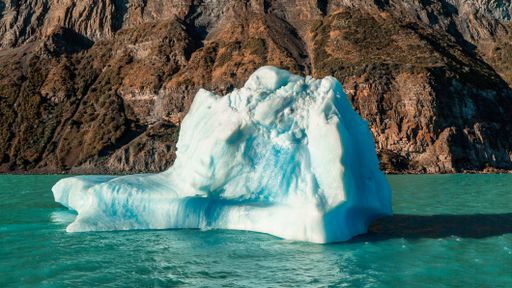 Floating iceberg on a lake in Patagonia, Argentina, with mountains and clouds in the background.