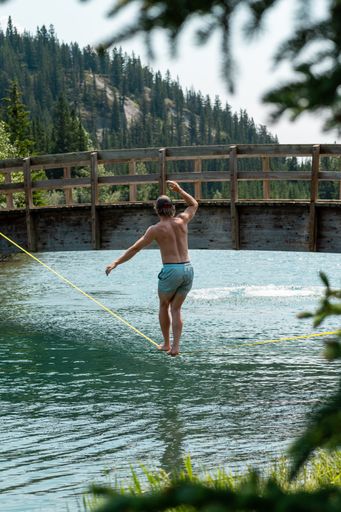 A vertical shot of the man in blue shorts walking on the rope above the river.
