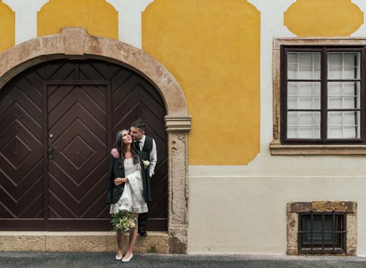 Beautiful bride and groom standing in front of wooden door on yellow building at Gornji Grad in Zagreb, Croatia.