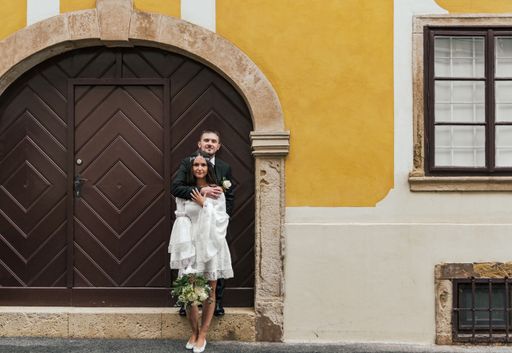 Beautiful bride and groom standing in front of wooden door on yellow building at Gornji Grad in Zagreb, Croatia.