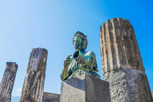 Ancient statue and columns under a clear blue sky in Pompeii, Italy, showcasing historical architecture and art.
