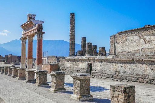 Ancient ruins of Pompeii with columns and a bright blue sky, showcasing historical architecture against a mountain backdrop.
