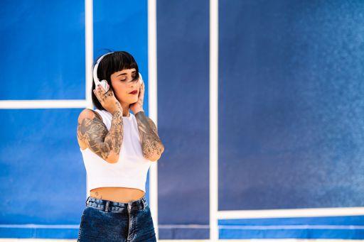 A young attractive caucasian female with tattoos listening to music with headphones and dancing