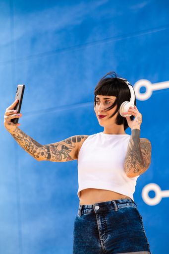 A young attractive caucasian female with tattoos listening to music with headphones and taking photos