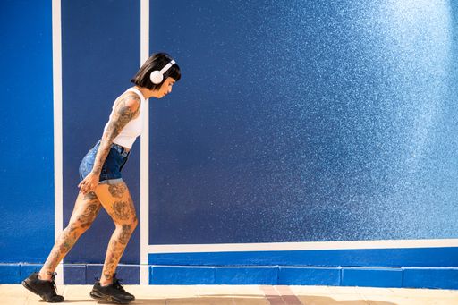 A young attractive caucasian female with tattoos listening to music with headphones and dancing