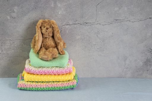 Stack of warm colorful baby sweaters, knitted clothes on a table. Homemade garment with a rabbit on top. Gray background with copy space.