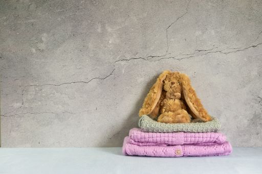 Cozy, warm pink and grey baby sweaters, knitted clothes on a table. Stack of handmade garment with a rabbit on top. Gray background with copy space.