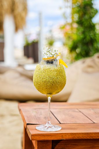 A view of a yellow cocktail in a glass on a wooden table near the coast