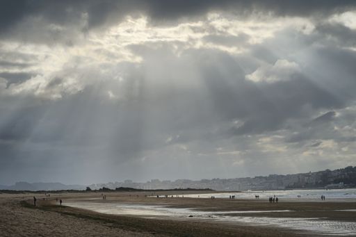 A beautiful shot of a beach under the cloudy skies with the sun coming out from them