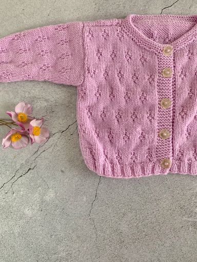 Cozy, warm pink baby sweater, knitted clothes on a table. Handmade garment and a few flowers. Gray background with copy space and place for text.