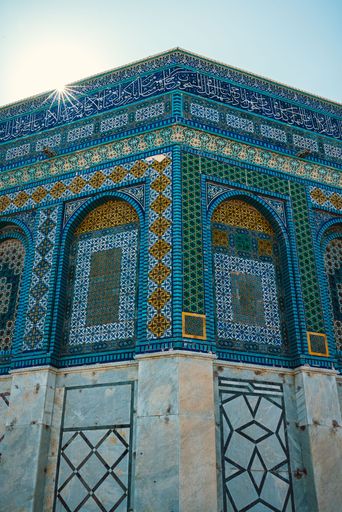 Close-up of intricate tile work on the Dome of the Rock in Jerusalem, showcasing vibrant blue and gold patterns under a clear sky.
